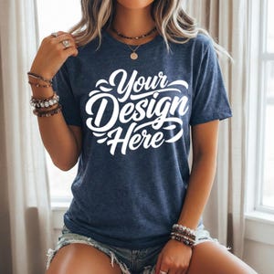May include: A navy blue t-shirt with the text "Your Design Here" in white script. The short-sleeved shirt is made of a soft material and is suitable for custom designs. The shirt is worn with denim shorts.