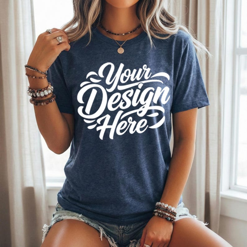 May include: A navy blue t-shirt with the text "Your Design Here" in white script. The short-sleeved shirt is made of a soft material and is suitable for custom designs. The shirt is worn with denim shorts.