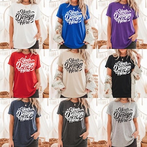 Puede incluir: Colección de nueve camisetas en varios colores: blanco, azul, morado, rojo, beige, negro, marino, carbón y gris. Cada camiseta presenta el texto "Your Design Here" en una escritura estilizada, ideal para diseños personalizados.