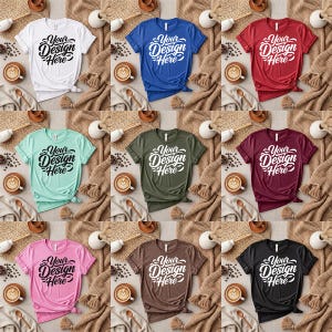 May include: A collection of t-shirts in various colors, including white, blue, red, teal, olive green, pink, brown, burgundy, and black. Each shirt features the text "Your Design Here" in a stylized font. The shirts are arranged on a textured background with coffee cups and decorative elements.