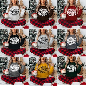 May include: A collection of women's sweatshirts in various colors, each with the text "Your Design Here" in a script font. The models are wearing matching red and black plaid pajama pants and holding Santa mugs.