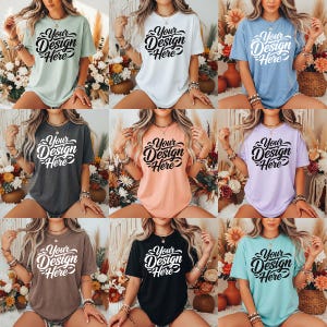 May include: Nine t-shirts in a range of colours, each with the text "Your Design Here" in a decorative script. The shirts are modelled, displaying the available colour options. The t-shirts are a casual style.