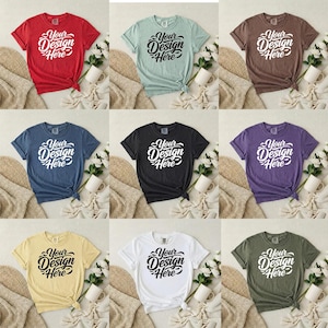 May include: Nine different colored t-shirts, each with the text "Your Design Here" in a white script font. The shirts are in various colors, including red, green, brown, blue, black, purple, yellow, white, and olive green. Each shirt is styled with a knot at the bottom.