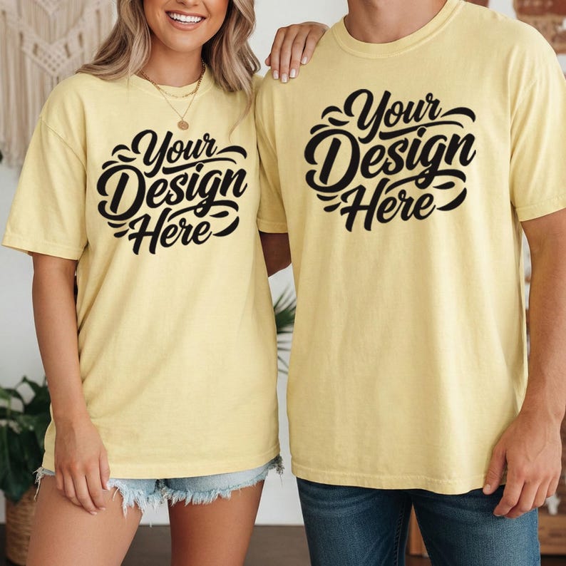 May include: Two yellow t-shirts with the text "Your Design Here" in a black, stylized font. The shirts are short-sleeved and appear to be made of a soft material. The shirts are worn by two people.