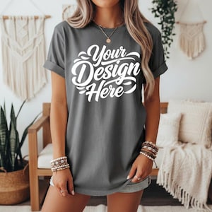 May include: A gray t-shirt with rolled-up sleeves featuring the text "Your Design Here" in a white, cursive font. The shirt is worn by a person with blonde hair, accessorized with bracelets and a necklace.