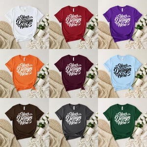 Könnte beinhalten: Neun T-Shirts in verschiedenen Farben, darunter Weiß, Rot, Lila, Orange, Burgunder, Hellblau, Braun, Grau und Grün. Jedes Shirt zeigt den Text "Your Design Here" in einer stilisierten Schriftart.