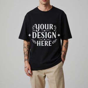 Pode incluir: Uma camiseta preta com o texto "YOUR DESIGN HERE" em letras brancas. O texto é rodeado por elementos decorativos, incluindo estrelas e acentos florais.