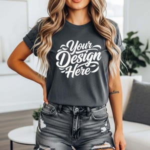 May include: Dark gray t-shirt with rolled sleeves and the text "Your Design Here" in white script. The model is wearing denim shorts. The shirt is a mockup for custom designs.