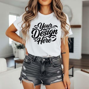 May include: White t-shirt with the text "Your Design Here" in a black, cursive font. The shirt is being worn with denim shorts. The overall aesthetic is casual and modern, suitable for design mockups.