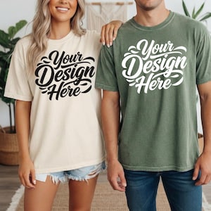 May include: Two short-sleeved t-shirts, one cream-colored and the other olive green, each with the text "Your Design Here" in a stylized script. The shirts are worn by two people, and the overall style is casual and relaxed.