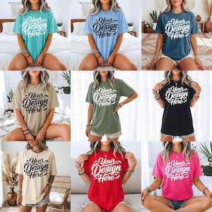 May include: A collection of nine short-sleeved t-shirts in various colors, including teal, light blue, navy, tan, olive green, black, cream, red, and pink. Each shirt features the text "Your Design Here" in a stylized script.