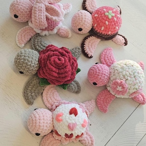 Peut inclure: Plusieurs tortues faites à la main au crochet, dans des tons de rose, de gris et de blanc. Certaines tortues présentent des motifs floraux, dont une grande rose rouge et de plus petites fleurs. Les tortues sont douces et moelleuses, parfaites pour une chambre d'enfant.