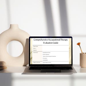 May include: A laptop displays a "Comprehensive Occupational Therapy Evaluation Guide" on its screen. The laptop is open on a white surface, next to a beige vase and a small container holding a paintbrush.