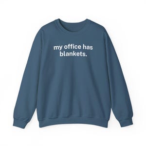 May include: A blue sweatshirt with the phrase "my office has blankets" printed in white. The crew neck sweatshirt is a solid color and has long sleeves. The text is centered on the chest.