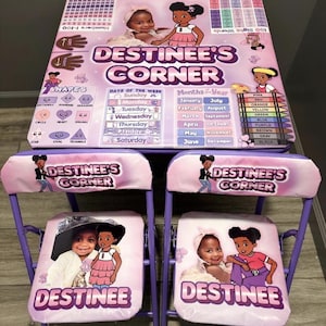 Könnte beinhalten: Ein Kinderspielset mit Tisch und zwei Stühlen. Das Set ist hauptsächlich hellviolett und rosa und zeigt den Text "DESTINEE'S CORNER" sowie Bilder eines Kindes und Cartoon-Illustrationen. Der Tisch enthält Bildungselemente.