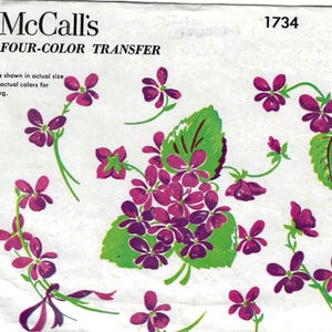 May include: Vintage McCall's Four-Color Transfer pattern featuring a floral design of purple flowers, green leaves, and stems. The text "McCall's" and "1734" are visible. The design is shown in actual size and colors for stamping.