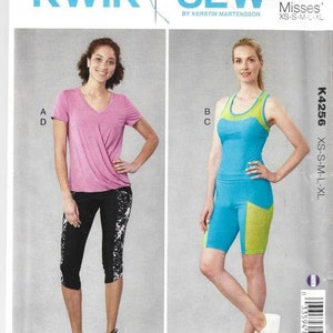 May include: Sewing pattern for two athletic outfits. The first outfit is a pink top with a v-neck and black and white leggings. The second outfit is a blue tank top with a green accent and blue and green leggings. The pattern is called "Kwik Sew" and the number is "K4256".