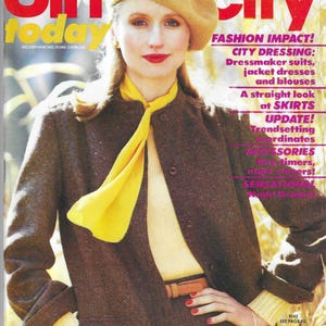 May include: A magazine cover featuring a woman wearing a brown jacket, a yellow scarf, and a brown beret. The magazine is titled "Simplicity" and the cover text reads "Fashion Impact! City Dressing: Dressmaker suits, jacket dresses and blouses. A straight look at skirts. Update! Trendsetting coordinates. Accessories. Daytimers, night-timers! Sensational Night Dresses."