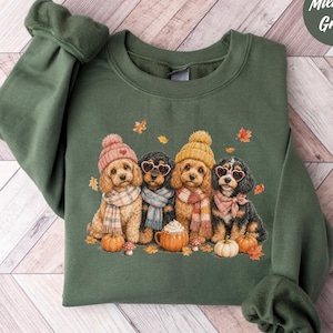 May include: A military green crewneck sweatshirt featuring a graphic of four puppies wearing knit hats and scarves, with two puppies wearing heart-shaped glasses. The design includes small pumpkins and autumn leaves, with the text Military Green.