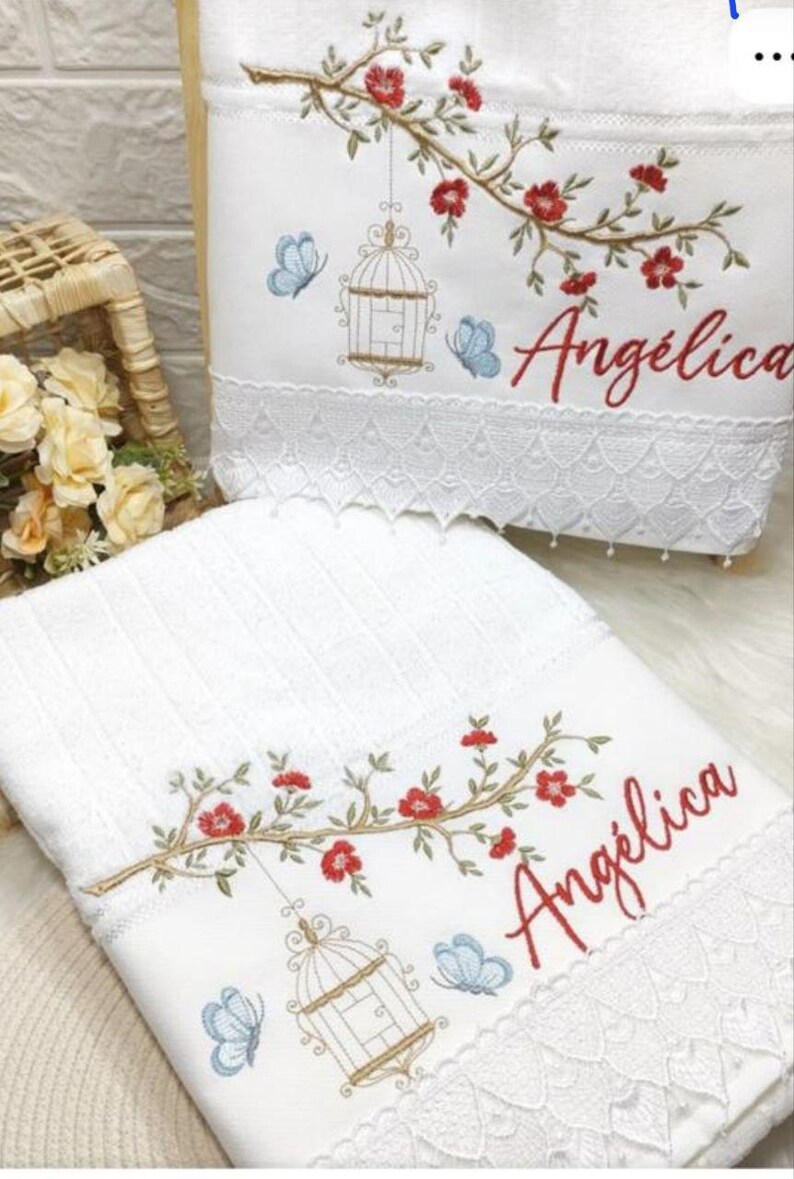 Puede incluir: Toallas blancas bordadas con dise&ntilde;os florales y de jaulas para p&aacute;jaros. Las toallas presentan flores rojas, mariposas azules y el nombre "Ang&eacute;lica" en escritura roja. El borde inferior tiene un ribete de encaje decorativo.