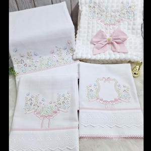 Puede incluir: Juego de ropa de cama para beb&eacute; blanco con bordados florales en colores pastel. El juego incluye un edred&oacute;n con un gran lazo rosa y varias mantas bordadas con ribete de encaje. El bordado presenta flores, mariposas y cintas.
