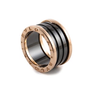 May include: A wide band ring crafted from rose gold and black ceramic. The ring features a multi-layered design with two rose gold edges engraved with the text BVLGARI and a central black ceramic band, creating a bold and structured appearance.