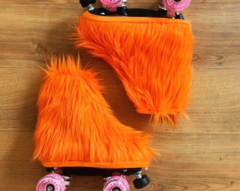 Può includere: Un paio di pattini a rotelle con coperture in finta pelliccia arancione brillante e pelosa. I pattini hanno basi nere, ruote rosa e fermi neri. Le ruote sono visibili e la pelliccia copre la parte dello stivale dei pattini.