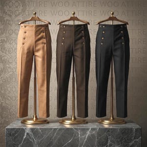 Può includere: Tre paia di pantaloni a vita alta esposti su supporti dorati. I pantaloni sono disponibili in beige, marrone scuro e nero, ciascuno caratterizzato da una chiusura a doppio petto con sei bottoni metallici disposti in due file verticali.