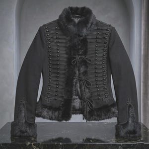 May include: A black jacket featuring a high collar trimmed with faux fur, long sleeves with fur cuffs, and a front closure with three cord ties. The front is decorated with rows of black braided cord trim and small black buttons on both sides.