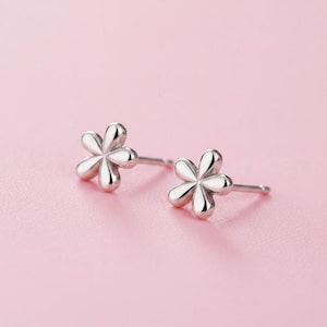 May include: A pair of silver-toned stud earrings shaped like five-petaled flowers. Each earring features a smooth, polished metallic finish with rounded petals radiating from a central point, complete with a standard post backing for secure attachment.