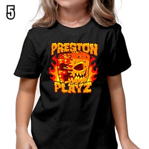 K&ouml;nnte beinhalten: Schwarzes T-Shirt mit dem Text "PRESTON PLAYZ" in Orange und Gelb und einer feurigen Grafik eines pixeligen Sch&auml;dels. Die Zahl "5" befindet sich in der oberen linken Ecke.
