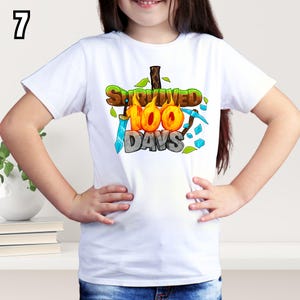 K&ouml;nnte beinhalten: Wei&szlig;es T-Shirt mit dem Text "Survived 100 Days" in einem farbenfrohen Cartoon-Design. Die Grafik enth&auml;lt ein Schwert, eine Spitzhacke und Bl&auml;tter. Die Zahl "7" befindet sich in der oberen linken Ecke.