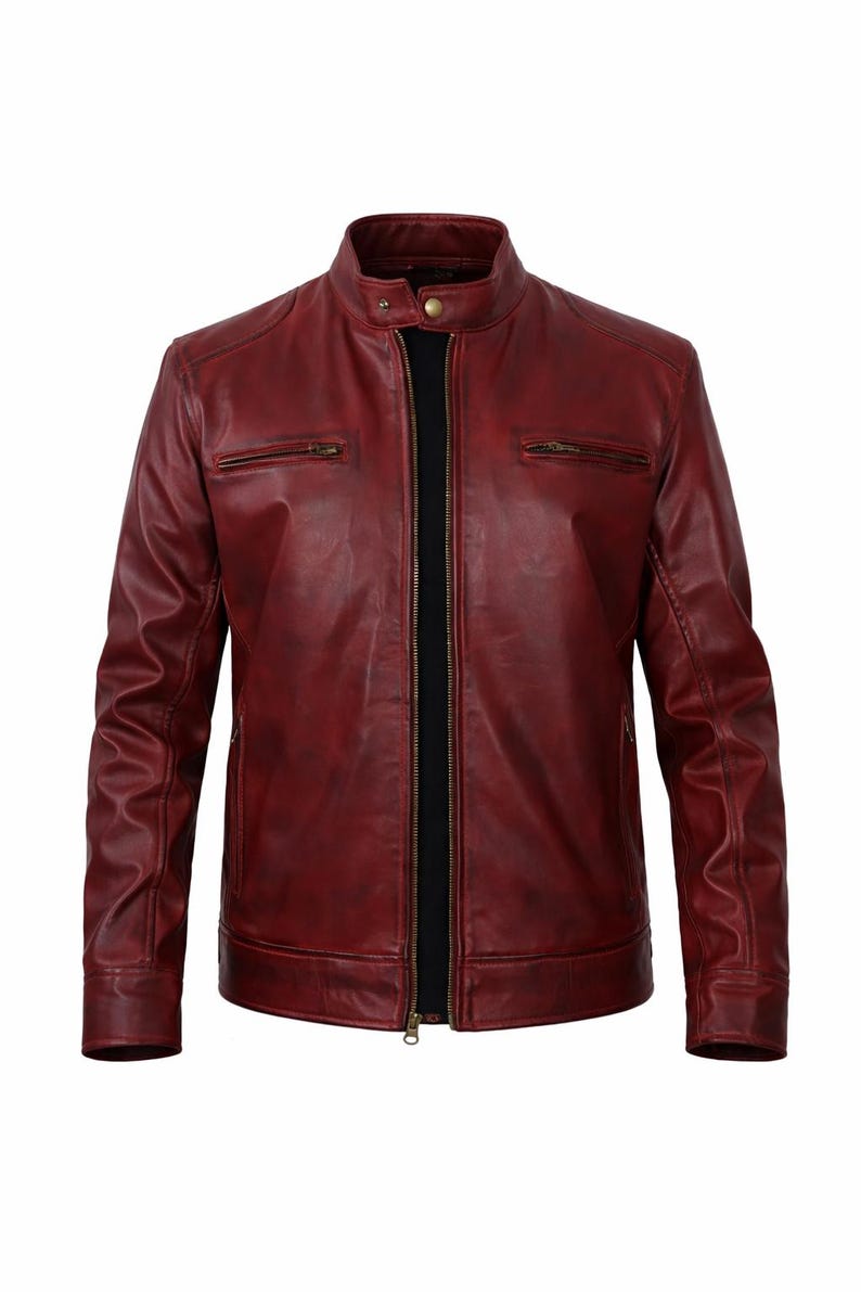 A burgundy leather jacket with a stand-up collar and a front zip. The jacket features two zipped chest pockets and a black inner lining. The long sleeves have a classic design.