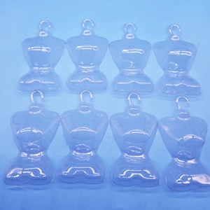 May include: Eight clear plastic miniature dress forms with hanger hooks. The forms are arranged in two rows of four against a light blue background. The forms are designed to display small garments.