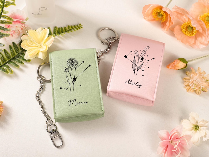 May include: Two keychains with matching cases. One is light green with a floral design and the name "Marcos". The other is pink with a floral design and the name "Shirley". Both have silver keyrings and chains.