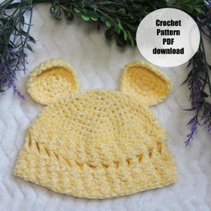 May include: A soft, yellow crochet hat with two attached ear-shaped accents. The hat is made of a plush, textured yarn. The image includes a circular graphic that reads "Crochet Pattern PDF download".