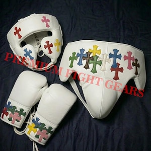 May include: White boxing equipment set with colourful cross designs. The set includes a head guard, boxing gloves, and a groin protector. The crosses are in various colours, including red, blue, yellow, and green.