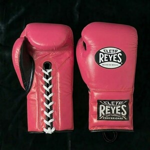 Peut inclure: Une paire de gants de boxe en cuir rose vif avec des lacets blancs sur la paume. Les gants présentent le logo noir et blanc Cleto Reyes sur le poignet et le dos de la main, avec l'inscription Hecho en Mexico clairement visible sur le cuir.