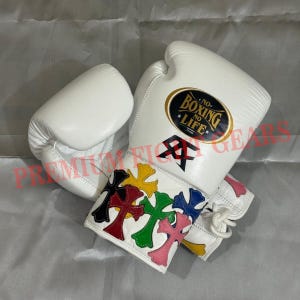 Puede incluir: Guantes de boxeo blancos con diseños de cruces de colores en la muñeca. Los guantes tienen el texto "BOXING NO LIFE" y un logotipo. Los guantes son de cuero.