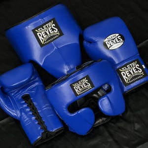 Peut inclure: Un ensemble d'équipement de boxe bleu roi comprenant deux gants de boxe à lacets et deux casques. Chaque article présente un écusson noir et blanc Cleto Reyes avec le texte Cleto Reyes Hecho en Mexico Professional imprimé sur le devant.