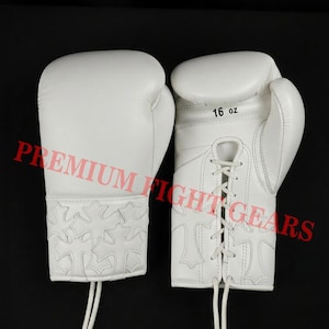May include: Pair of white boxing gloves with a lace-up closure. The gloves are marked as 16 oz. and feature a decorative pattern on the wrist cuff. The words "PREMIUM FIGHT GEARS" are printed across the image.