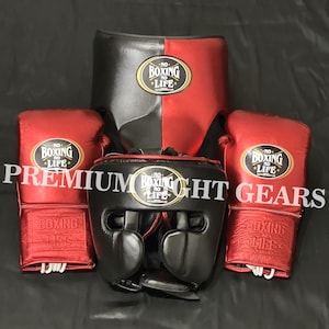 Op de afbeelding: Een set boksuitrusting bestaande uit twee metallic rode bokshandschoenen, een zwart-rode tok en een zwarte hoofdbeschermer. Elk item heeft een zwart-gouden ovaal embleem met de tekst NO BOXING NO LIFE. De tekst PREMIUM FIGHT GEARS is er overheen geplaatst.