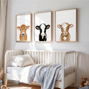 May include: Three framed watercolor paintings of calves. The first calf is brown and white, the second is black and white, and the third is brown and white. The paintings are hung on a white wall above a white crib.