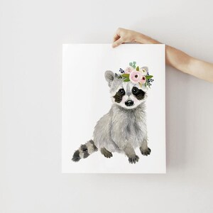 May include: A watercolor painting of a raccoon wearing a pink and green floral crown. The raccoon is sitting on a white background.