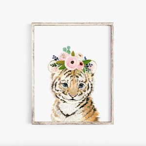 Pode incluir: Uma pintura em aquarela de um filhote de tigre usando uma coroa de flores rosa. O filhote de tigre tem listras marrons e pretas e olhos azuis. O fundo &eacute; branco.