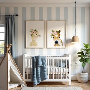 Pu&ograve; includere: Due stampe incorniciate di illustrazioni ad acquerello di animali che indossano corone di fiori. Le stampe sono appese a un muro a strisce blu chiaro e bianco sopra una culla bianca con una coperta blu. Una pianta in vaso si trova sul lato destro dell'immagine.