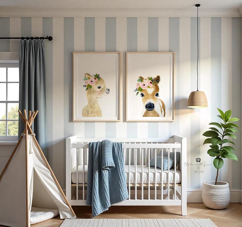 Pu&ograve; includere: Due stampe incorniciate di illustrazioni ad acquerello di animali che indossano corone di fiori. Le stampe sono appese a un muro a strisce blu chiaro e bianco sopra una culla bianca con una coperta blu. Una pianta in vaso si trova sul lato destro dell'immagine.