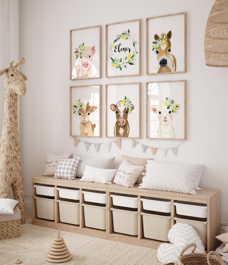 May include: A nursery room with a wooden storage bench with six drawers, a giraffe stuffed animal, a wooden stacking toy, and a set of six framed prints featuring watercolor illustrations of farm animals wearing flower crowns. The prints include a pig, a horse, a goat, a cow, a lamb, and a wreath with the name "Eleanor".