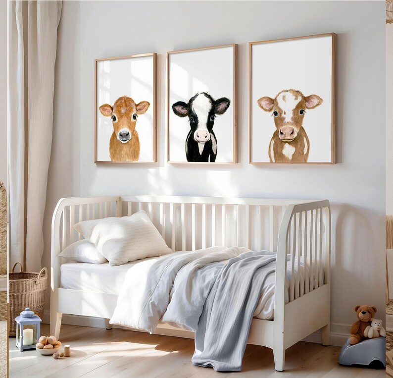 May include: Three framed watercolor paintings of calves. The first calf is brown and white, the second is black and white, and the third is brown and white. The paintings are hung on a white wall above a white crib.