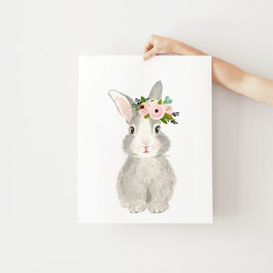May include: A gray bunny with a pink and green flower crown. The bunny is sitting on a white background.
